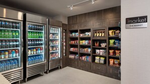 A grocery store interior with refrigerated beverage dispensers, snack shelves, and a sign reading "The Market". - Residence Inn by Marriott San Marcos (San Marcos)