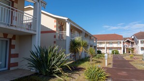 Un hotel de varios pisos con balcones, un sendero pavimentado y plantas tropicales.