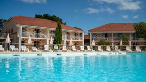 Una piscina con sillas de descanso y sombrillas, rodeada de edificios con balcones y un tejado de tejas rojas.