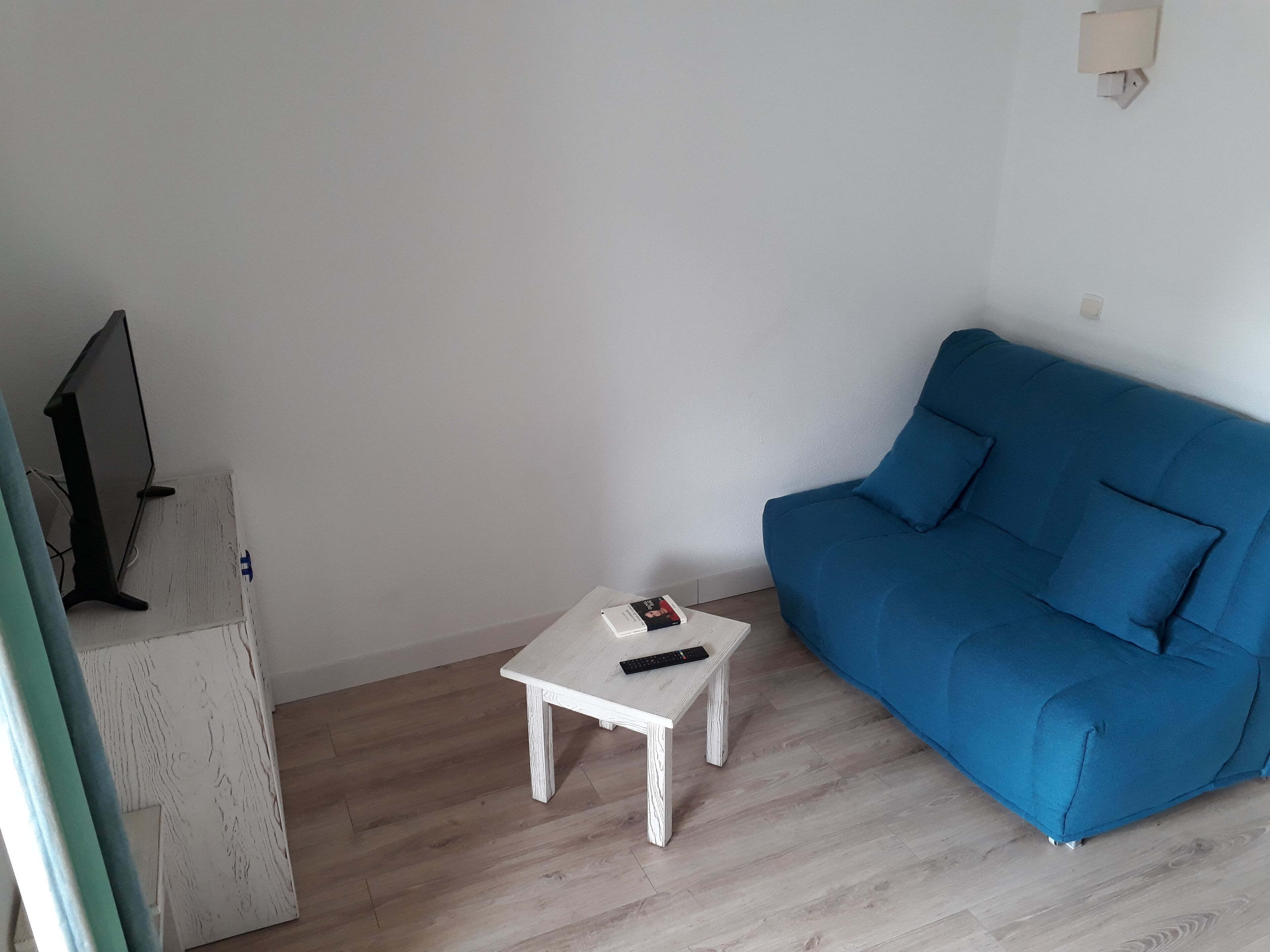 A room with a blue sofa, a white coffee table with a remote control, and a television on a wooden stand.