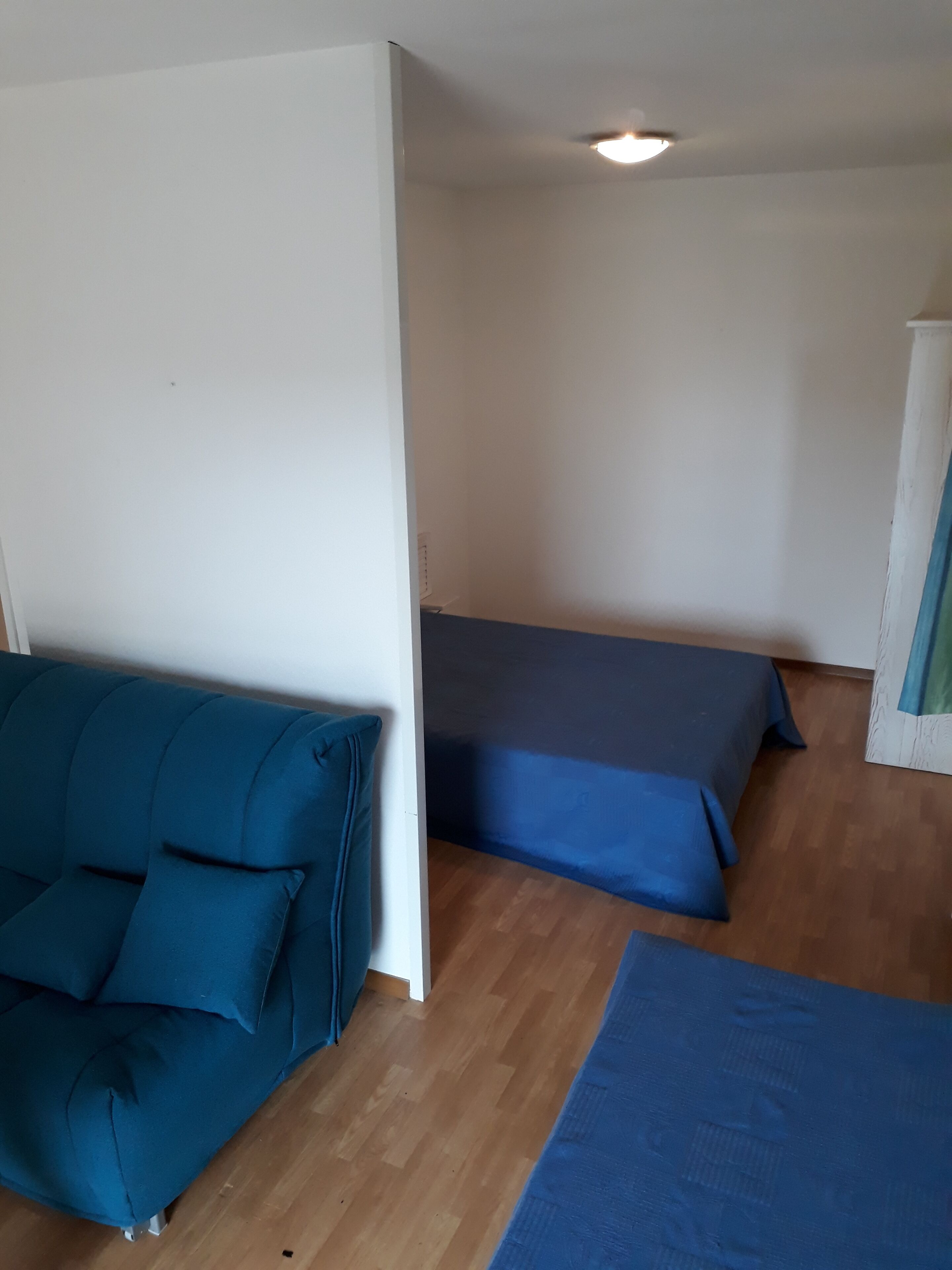 Une pièce avec un canapé bleu, un lit recouvert d’une courtepointe bleue et un plancher en bois.