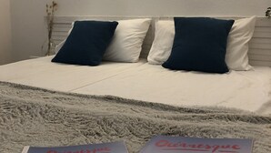 Habitación de hotel con una cama, dos almohadas, una mesita de noche con un florero y dos lámparas de pared.
