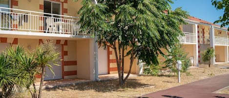 Un bâtiment avec un toit recouvert de tuiles rouges, un balcon avec des balustrades blanches et un arbre au premier plan.