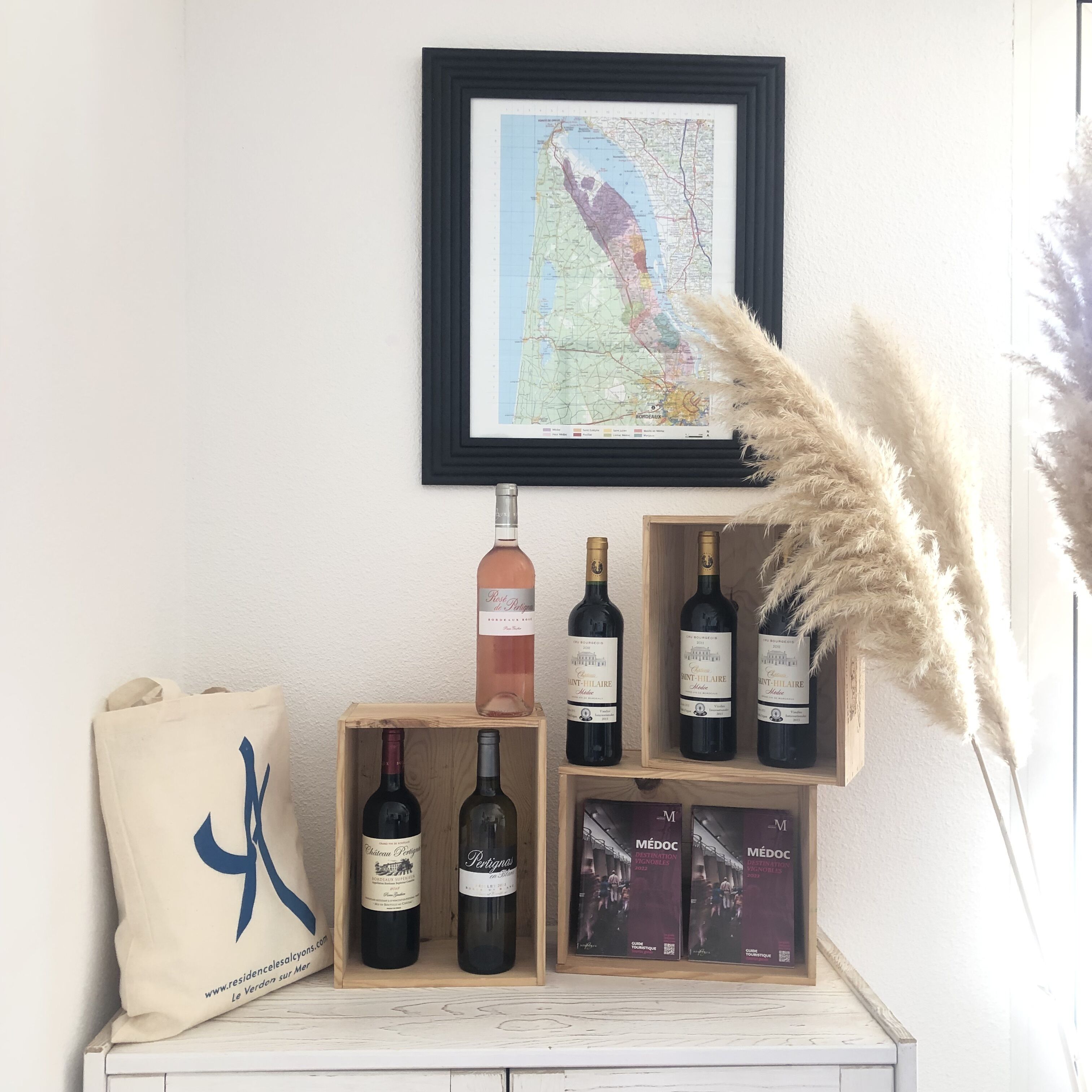 Un présentoir à vin en bois, avec des bouteilles, une carte et des plumes d’herbe de la pampa.