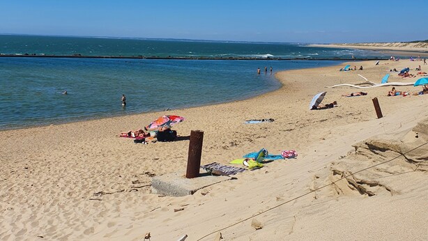 Una playa arenosa con cielo azul despejado, mar tranquilo y algunas personas.