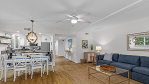 A modern kitchen with white cabinetry, a dining area with white chairs, a blue sofa, and a glass coffee table. - Seagrove Villa 5B by Deserving Vacations (Isle of Palms)