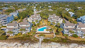 A coastal residential area with multiple two-story houses, a central swimming pool, and a rocky beach in the foreground. - Seagrove Villa 5B by Deserving Vacations (Isle of Palms)