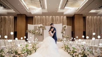 A wedding ceremony with a couple on an aisle decorated with floral arrangements and illuminated by chandeliers.