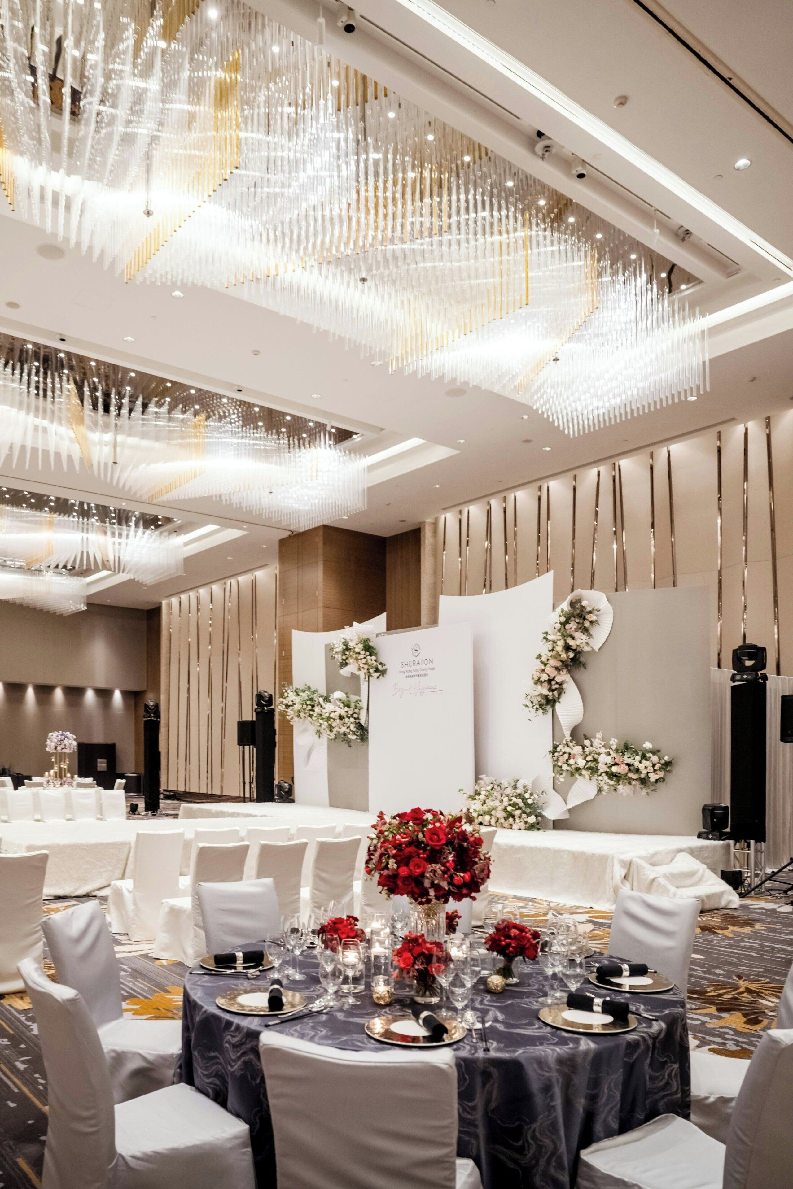 A banquet hall with round tables set for dining, elegant chandeliers, and floral decorations.