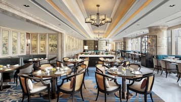 Un restaurant spacieux avec de hauts plafonds, des lustres et différents types de sièges, notamment des tables rondes et des banquettes.