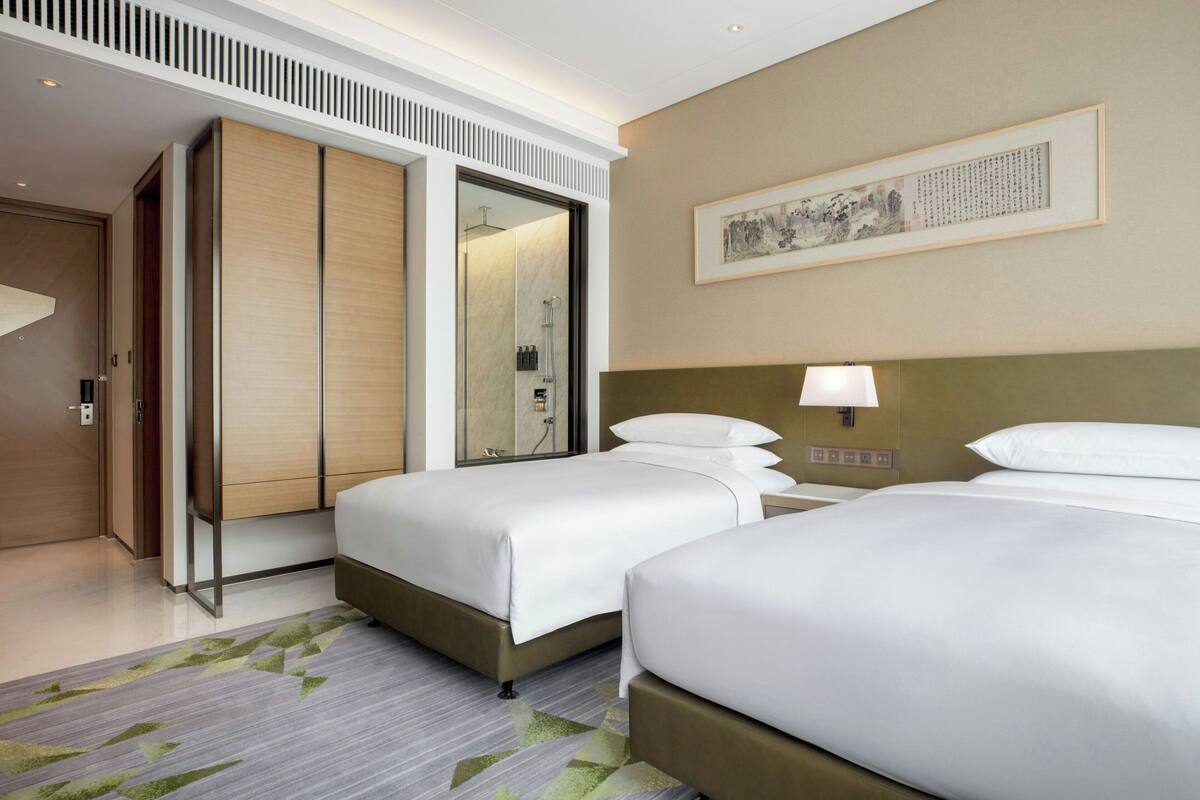 Une chambre d’hôtel avec deux lits, un dressing, une douche et une œuvre d’art encadrée au mur.