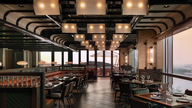 Een modern restaurant met hoge plafonds, hangende verlichting en uitzicht op de stad.
