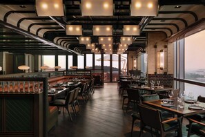 Un restaurante moderno con techos altos, iluminación colgante y vistas a la ciudad.