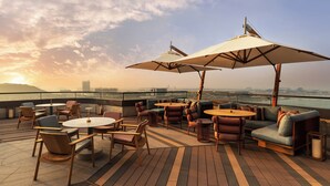 Een terras op het dak met buitenmeubilair, waaronder ronde tafels en banken, beschut onder grote parasols, met uitzicht op een stadsbeeld.