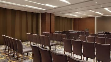 A conference room with rows of chairs, a patterned carpet, and recessed ceiling lighting.