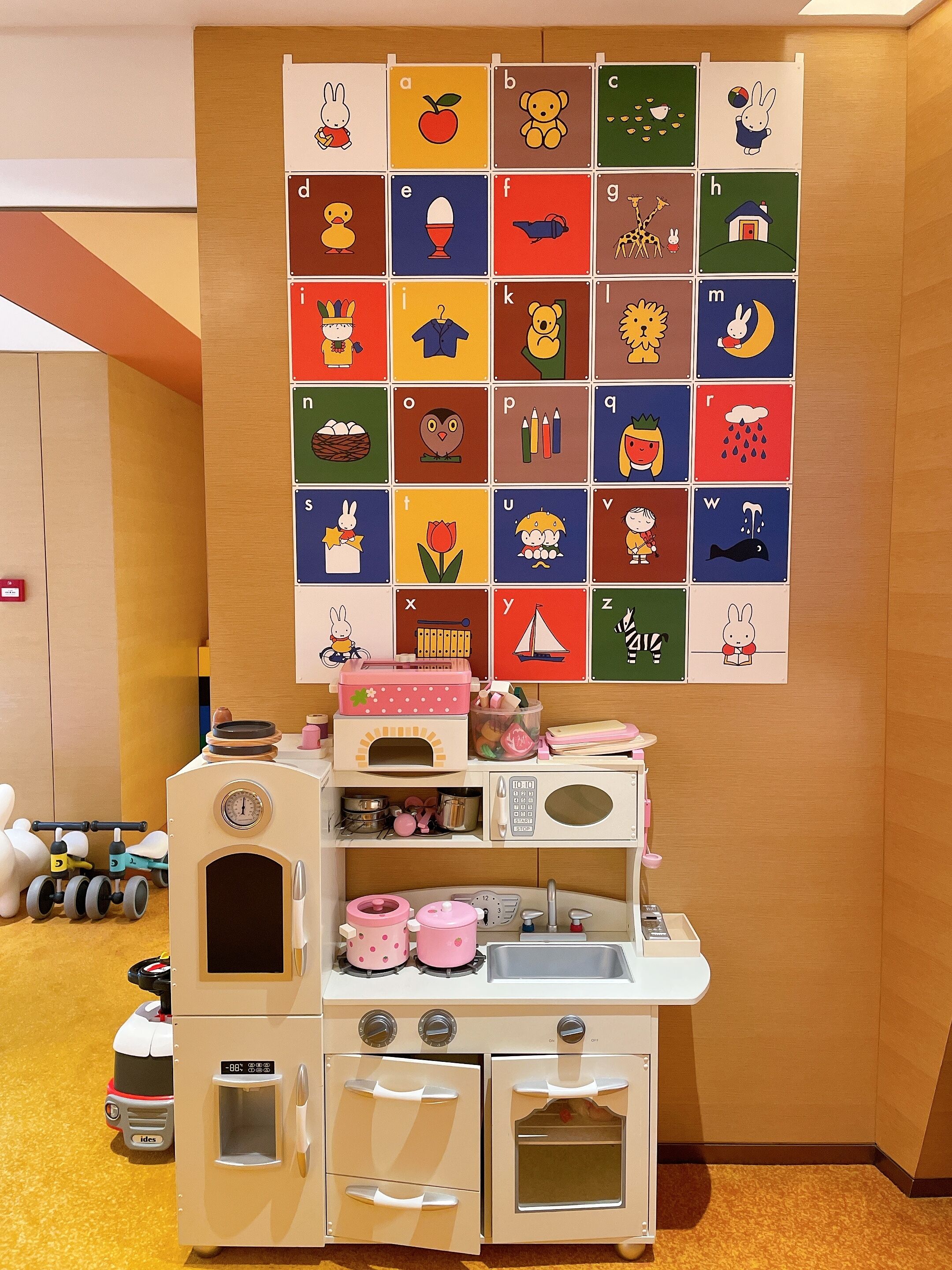 Une cuisine miniature pour enfants, avec un tableau de l’alphabet fixé au mur au-dessus.