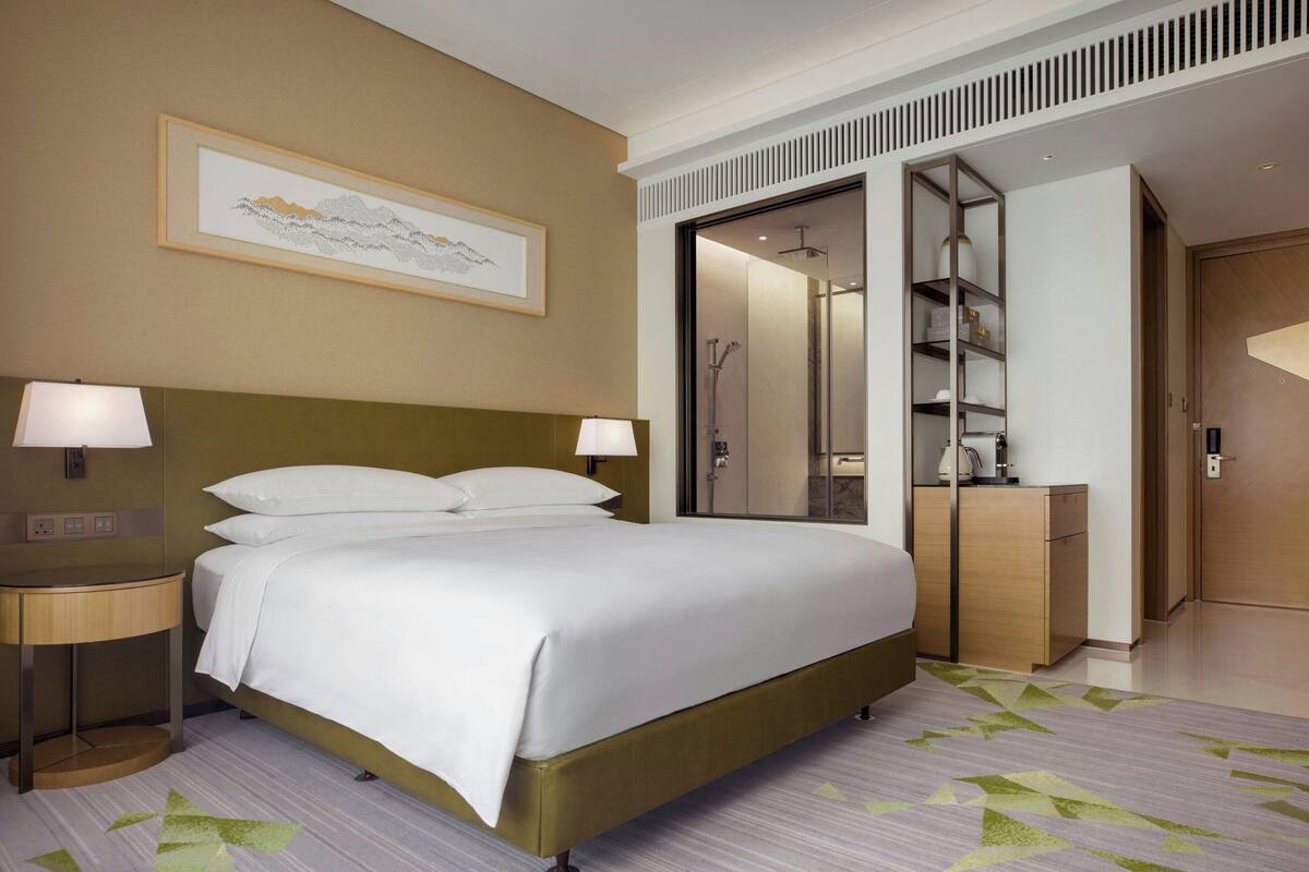 Une chambre d’hôtel avec un grand lit, deux tables de chevet avec des lampes, une armoire et un espace douche.
