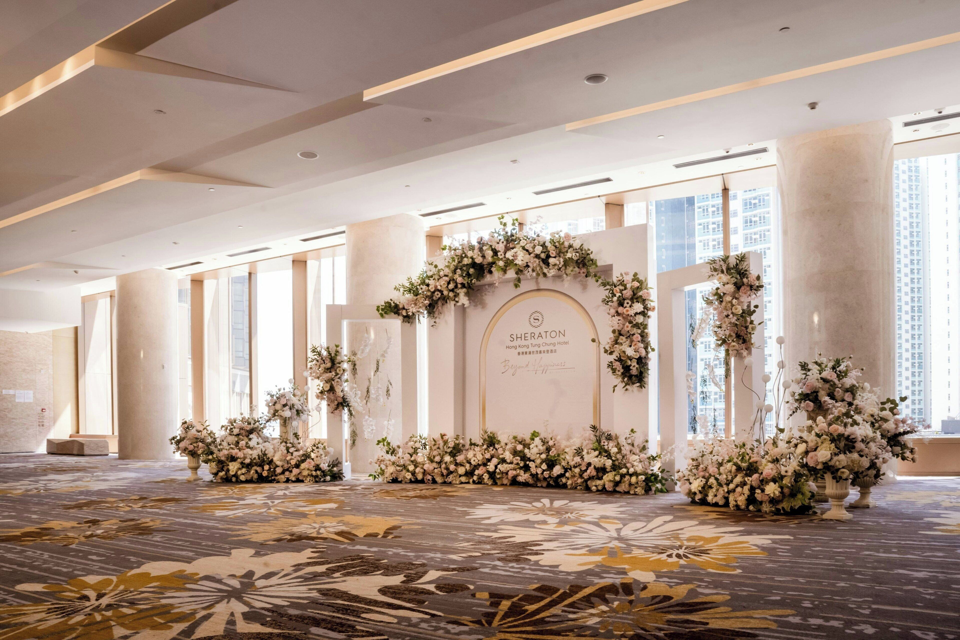 A spacious hotel lobby with a floral arrangement, a reception desk, and large windows.