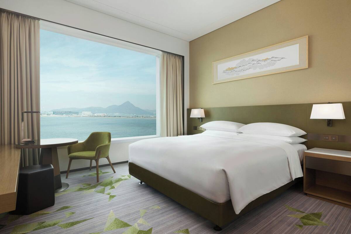 Une chambre d’hôtel avec un grand lit, un bureau, une chaise et une vue sur la mer et les montagnes.
