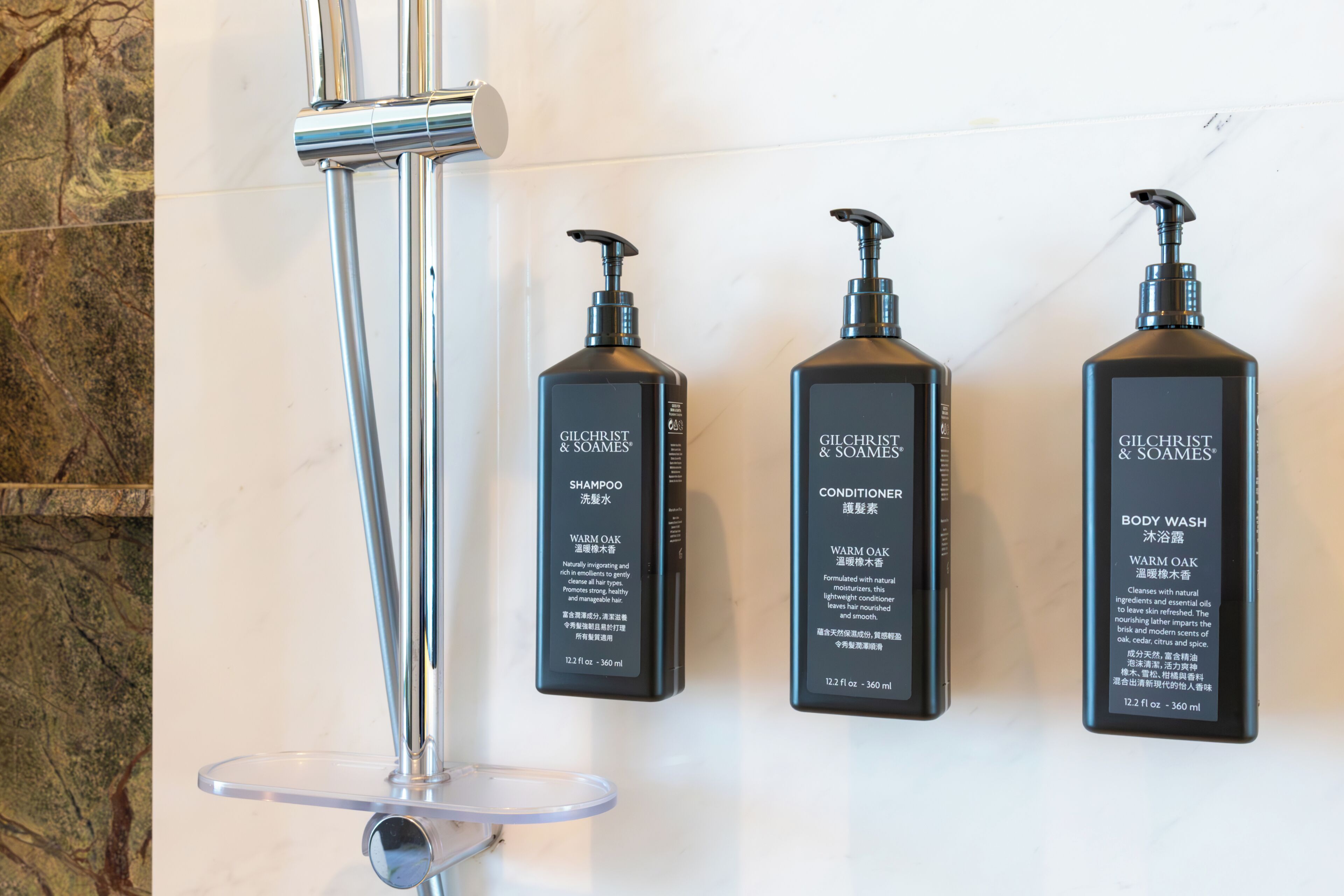 Three Gilchrist & Soames products: shampoo, conditioner, and body wash, mounted on a wall.