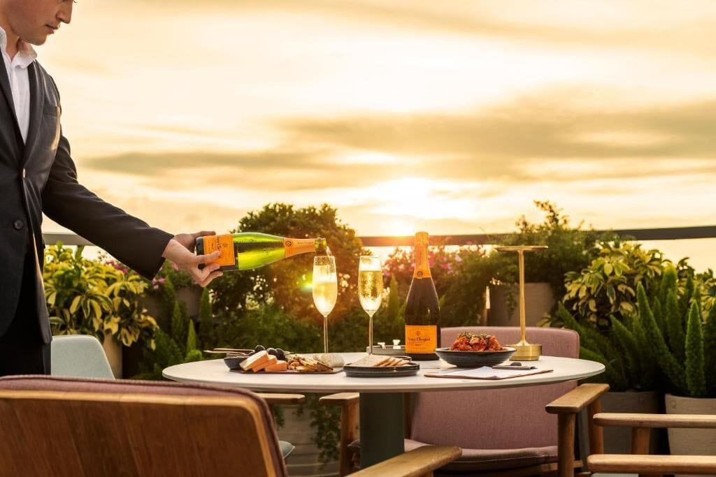 A table set for a meal with a bottle of champagne, glasses, and a bowl of food.