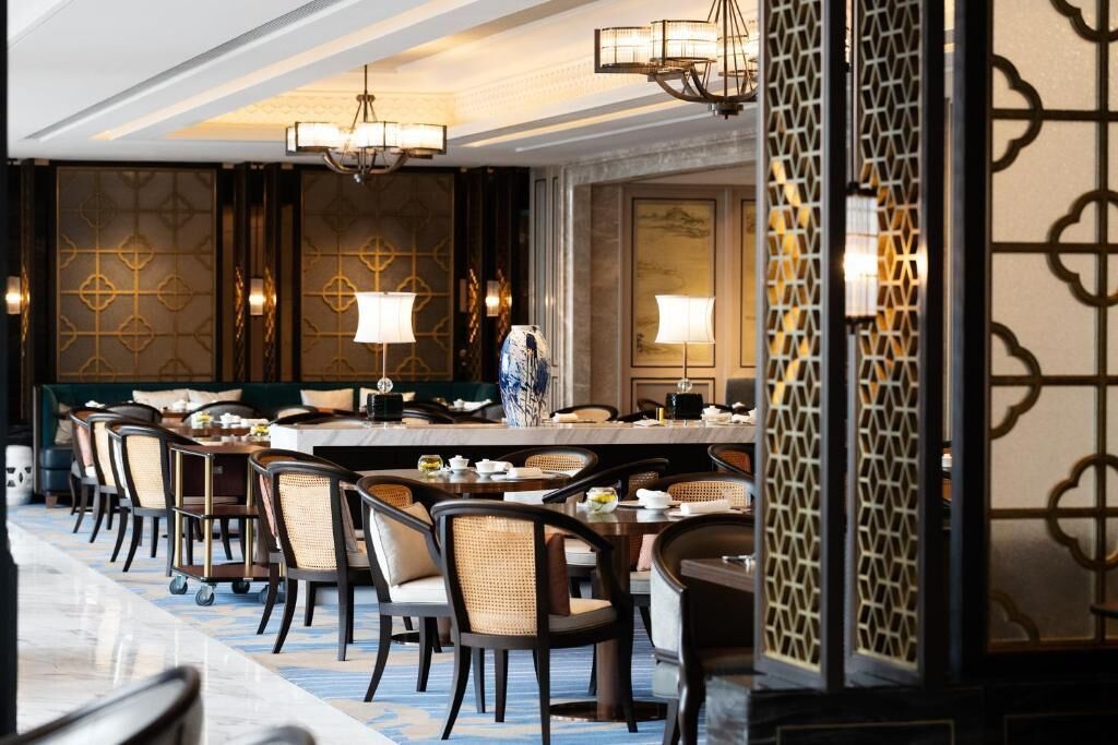 A formal dining area with multiple tables and chairs, elegant chandeliers, and decorative wall panels.