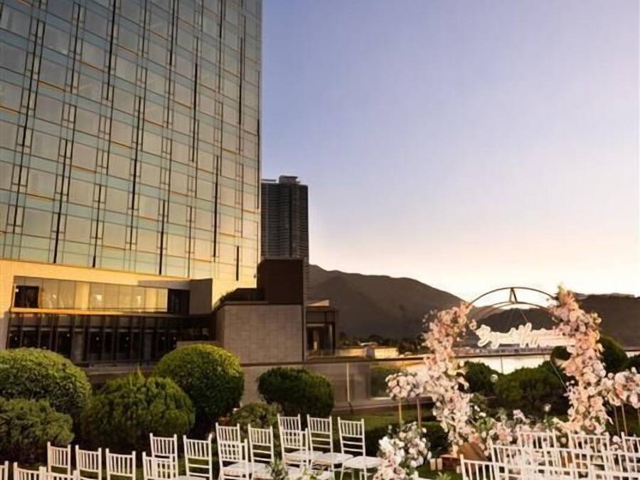 Un hotel Sheraton amb una zona d'estar exterior formal, amb cadires blanques i composicions florals, davant d'un cel blau i una muntanya.