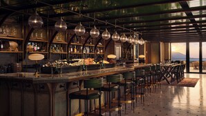 Een bar met een lange toonbank, verschillende barkrukken en hangende hanglampen.