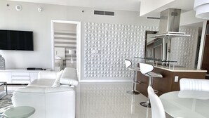 Una sala de estar moderna con un sofá blanco, una mesa de centro de vidrio y un comedor con sillas blancas y una mesa de vidrio.