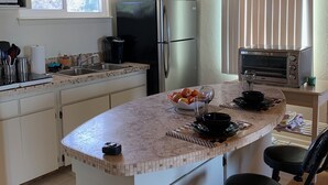 Una cocina con una isla grande, un refrigerador, un microondas y una ventana con persianas.