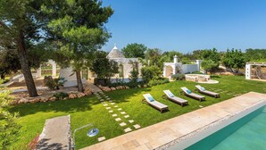 Zona junto a la piscina con sillones, un sendero de piedra y un edificio con techo cónico.