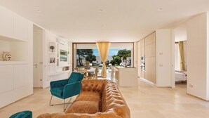 Una sala de estar moderna con sofá de cuero, sillas color turquesa y comedor con vistas al exterior.