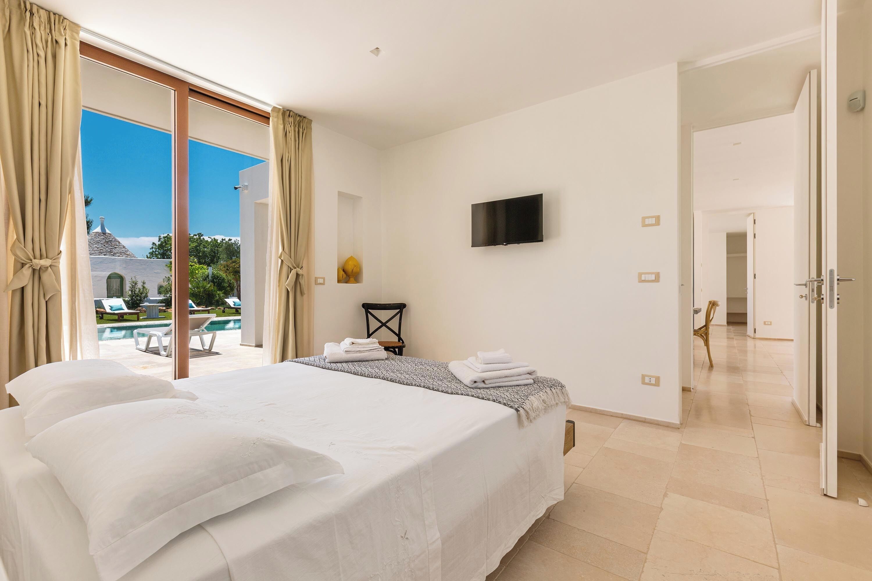 Habitación de hotel con una cama grande, un televisor de pantalla plana y vistas a una piscina y zona de estar exterior.