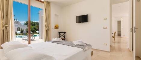 Habitación de hotel con una cama grande, un televisor de pantalla plana y vistas a una piscina y zona de estar exterior.
