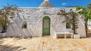 Un edificio blanco con puerta verde, dos ventanas pequeñas y techo de piedra.