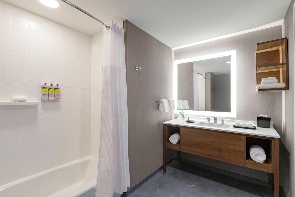 A modern bathroom with a bathtub, a vanity with a mirror, and a shower curtain.