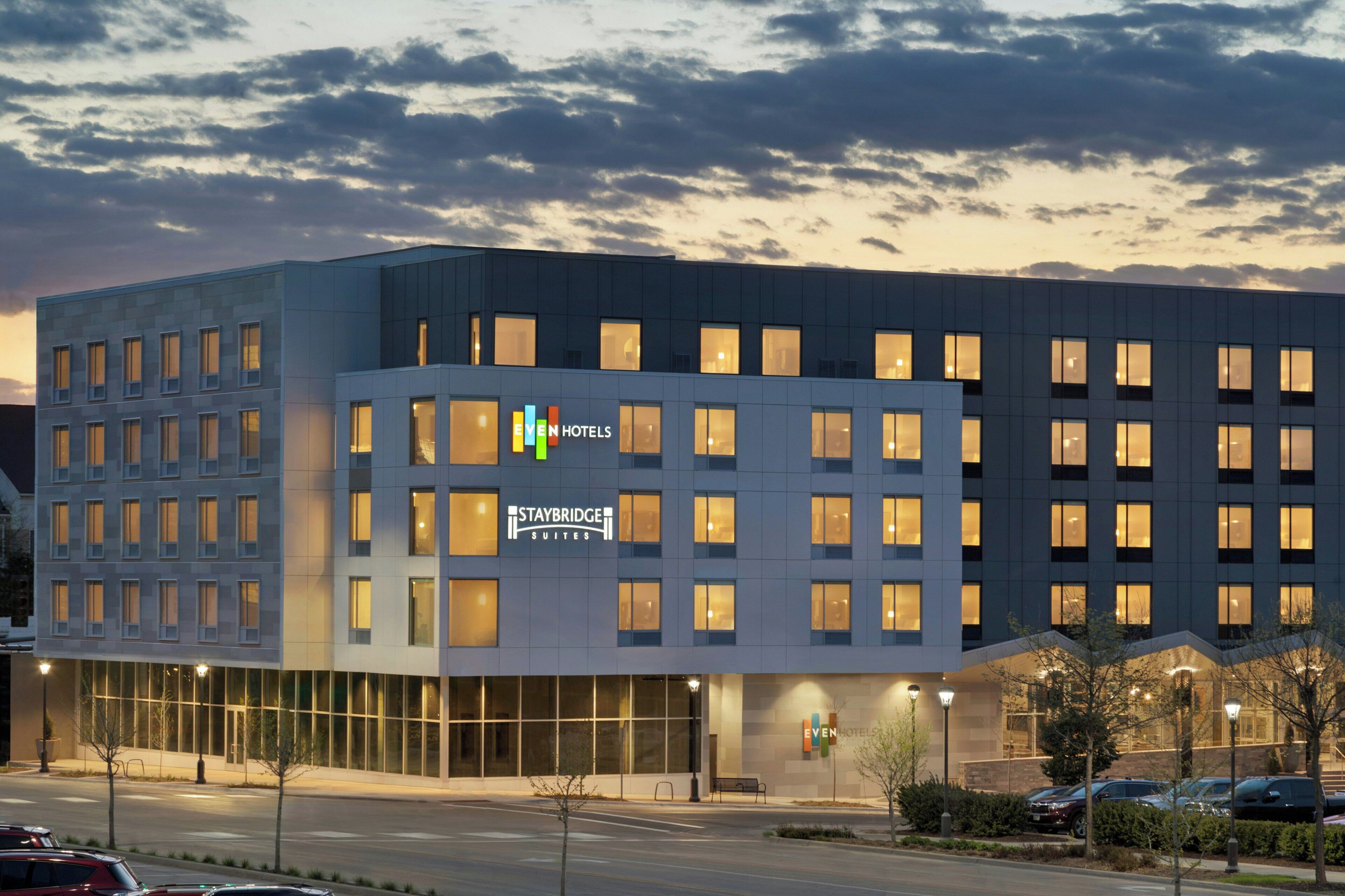 Un hotel de varios pisos con un letrero de Staybridge Suites, que presenta un diseño moderno con grandes ventanales y techo plano.