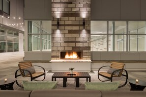 A modern outdoor seating area with a built-in fireplace, two wooden chairs, a table, and a sofa.