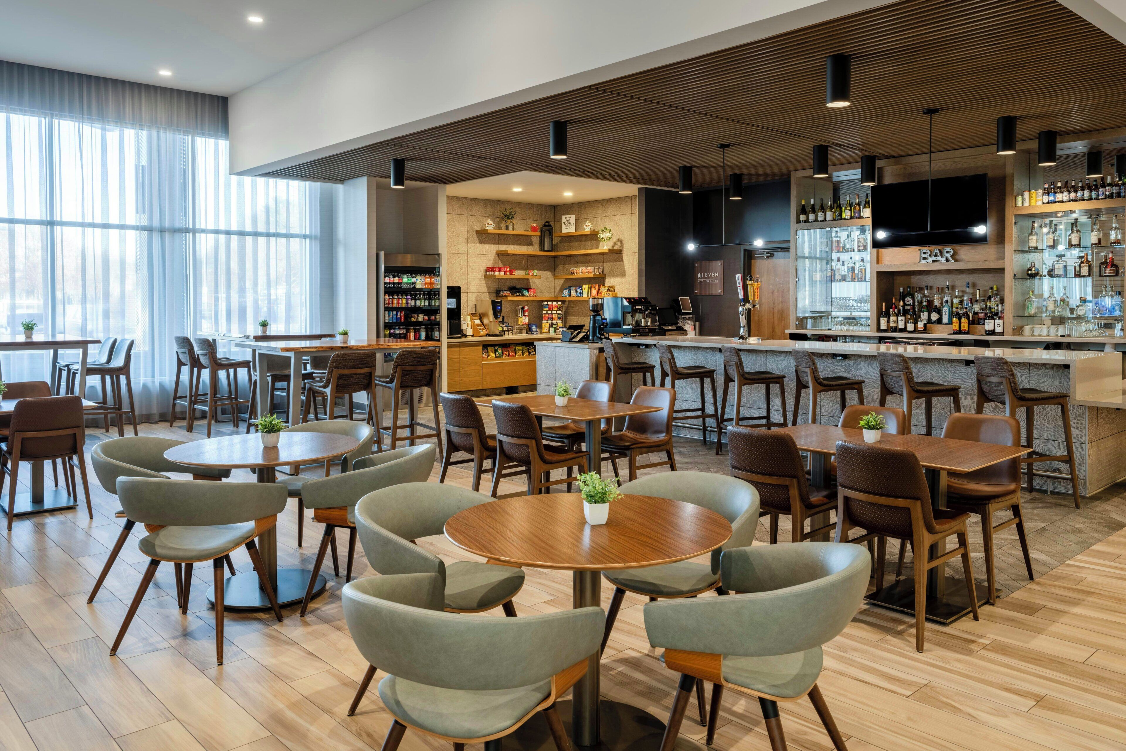 Un espace bar moderne offrant différents types de sièges, notamment des tables et des chaises rondes, un comptoir avec un assortiment de bouteilles et un appareil à café.
