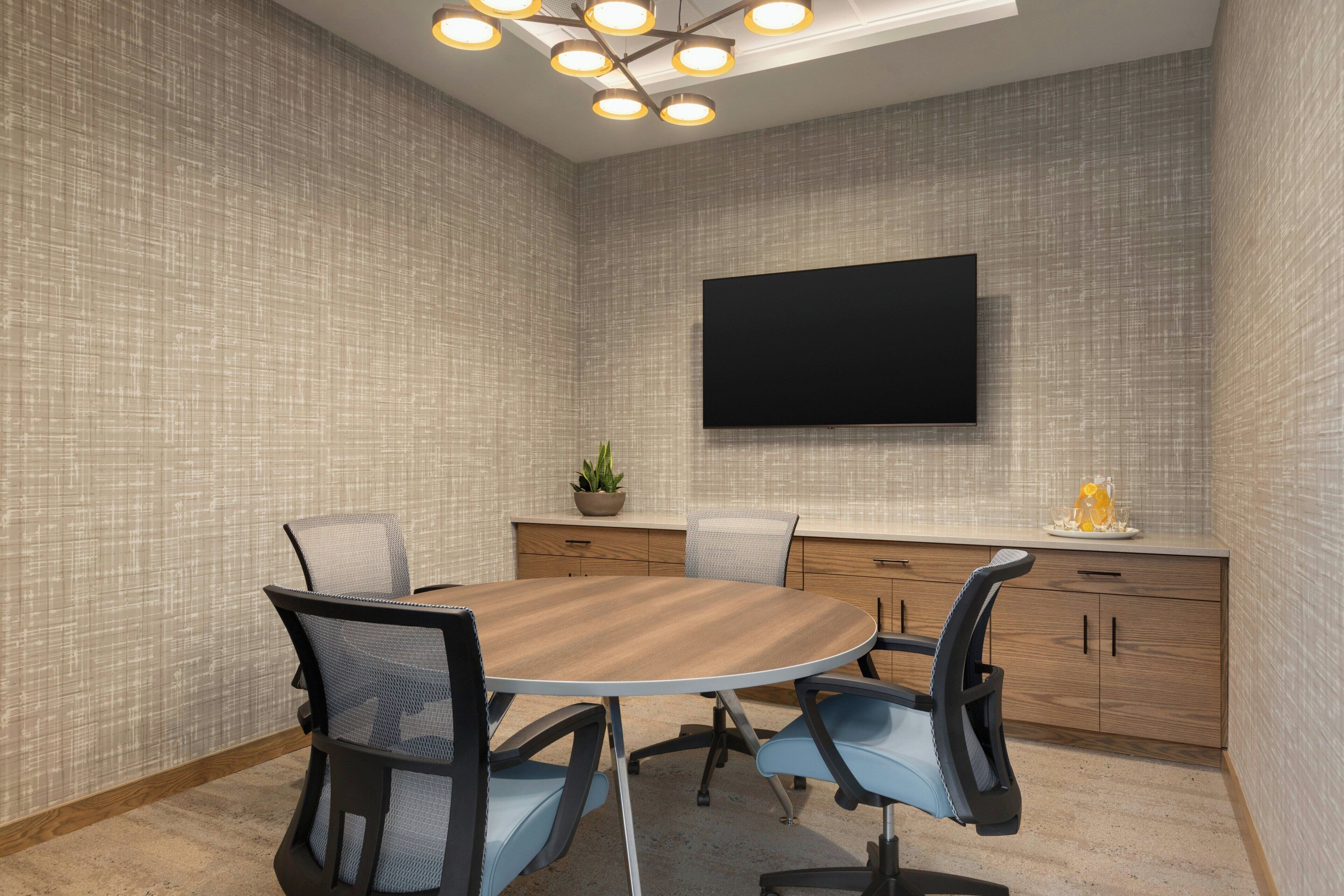 A conference room with a round table, chairs, a TV mounted on the wall, and a small plant on the counter.