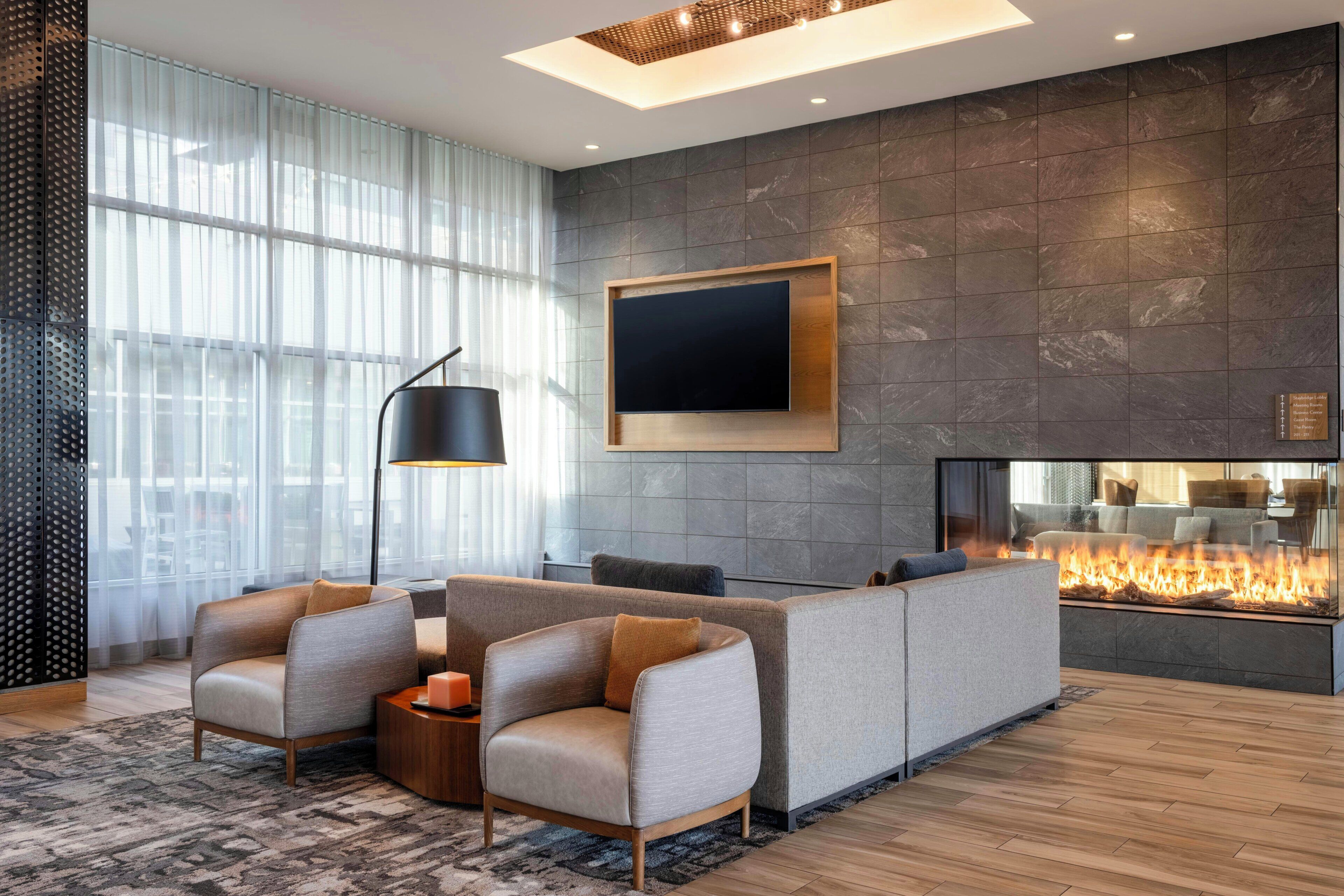A modern living room with a fireplace, comfortable seating, and a large window with sheer curtains.