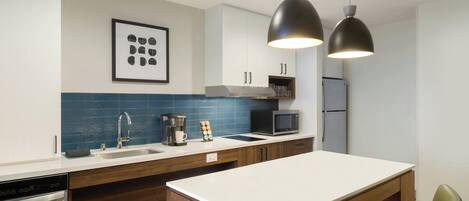 A modern kitchen with a white countertop, a coffee machine, a microwave, and a dishwasher.