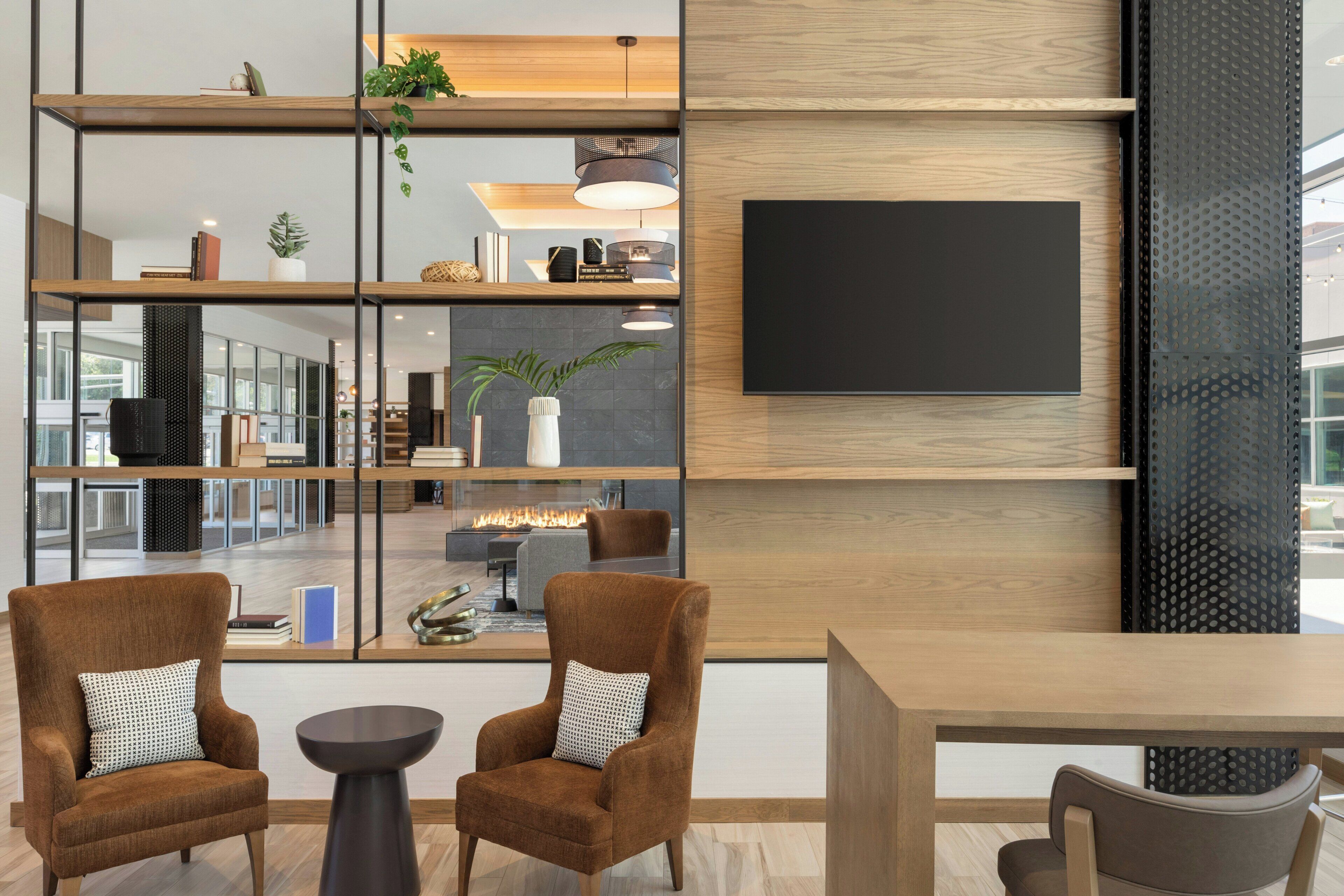 A modern interior with a wooden dining table, two brown armchairs, a black TV mounted on a wall, and a fireplace.