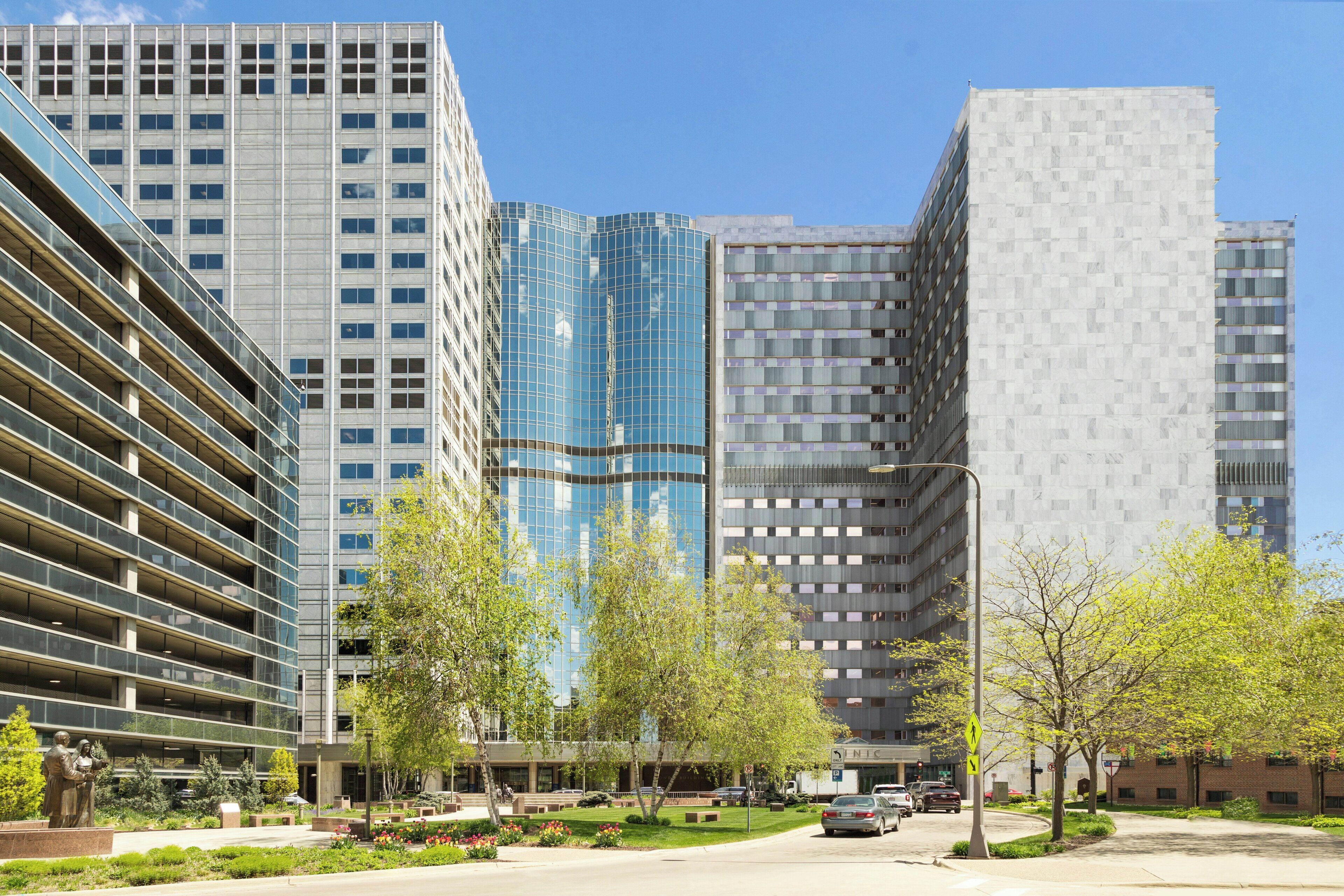 A modern urban street with tall buildings, a pedestrian walkway, and a parking area.