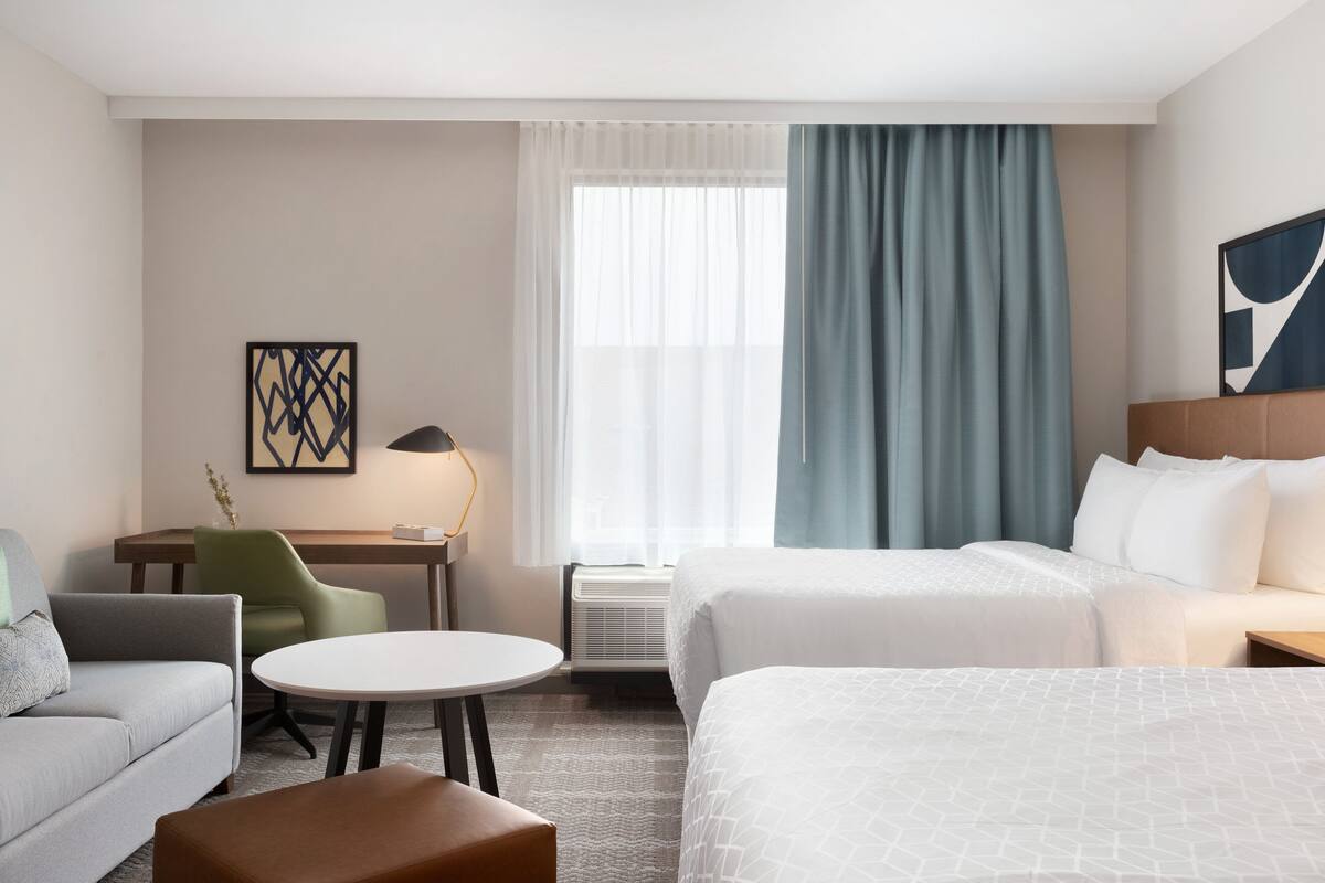 A hotel room with two beds, a desk, a chair, a round table, and a sofa.