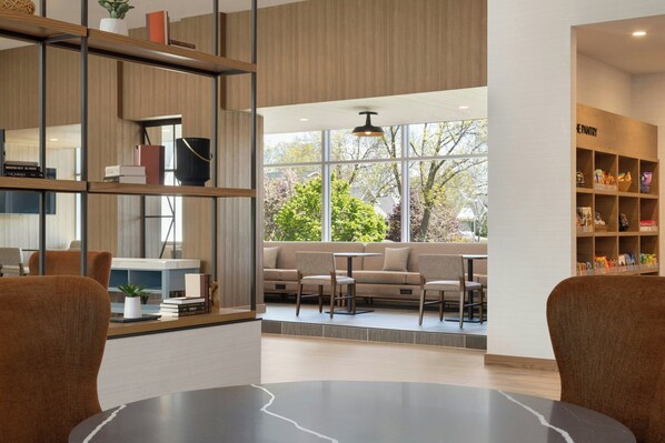 A modern interior with a seating area, a bookshelf, and a view through large windows.
