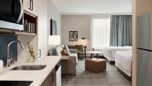Ein Hotelzimmer mit Küchenzeile, einem Bett, einer Couch, einem kleinen Tisch und einem Fenster mit Vorhängen.
