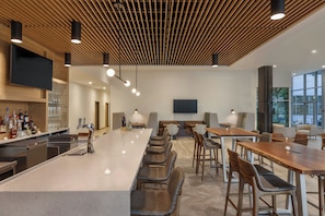 A modern bar area with a long counter, bar stools, and a television screen mounted on the wall.