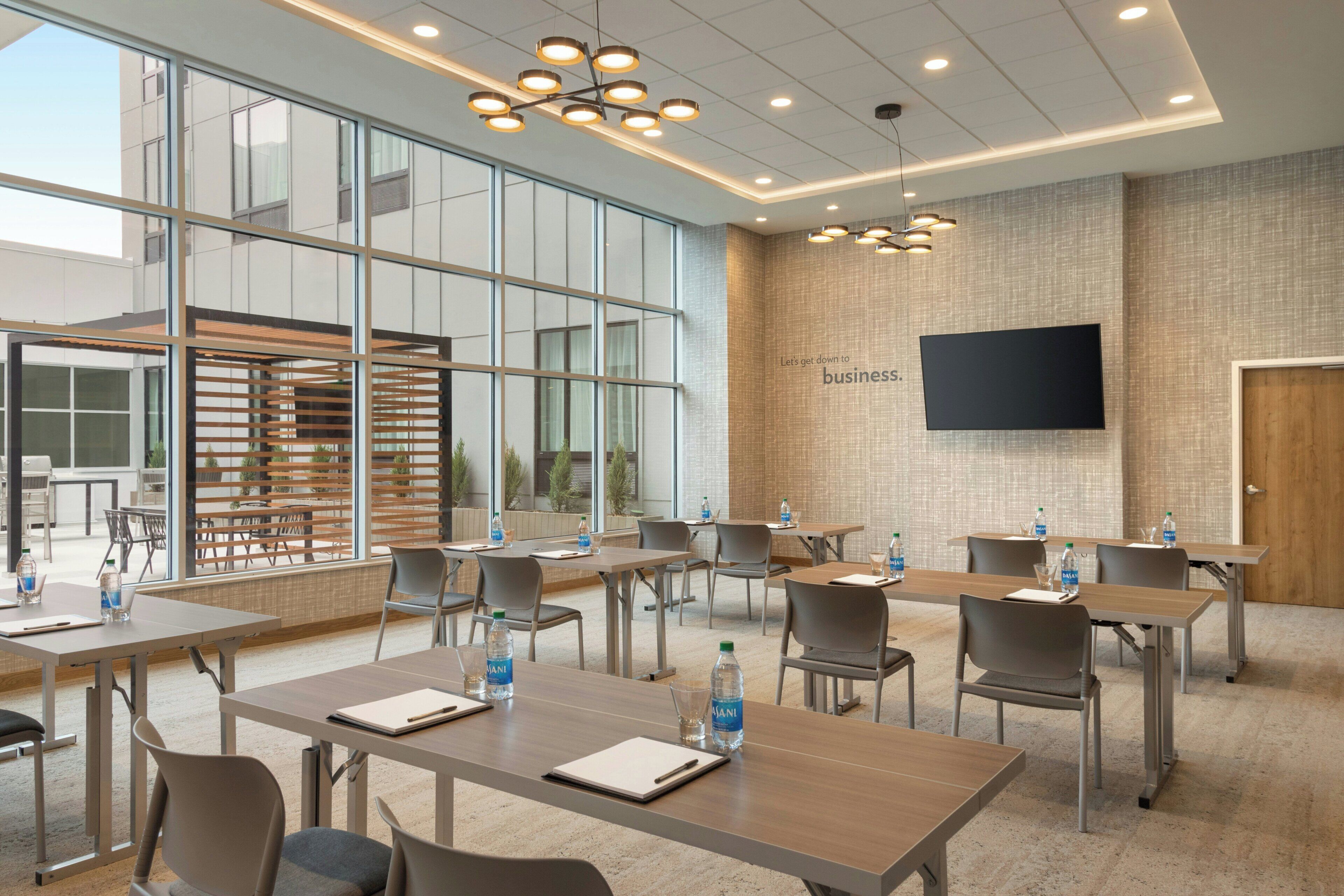 A conference room with tables, chairs, and a large flat-screen TV on the wall.