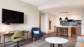 A modern living room with a TV, a desk, a green chair, a blue armchair, and a white round table.